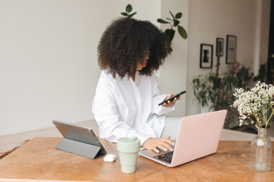 A Woman Holding a Cellphone and Typing on a Laptop